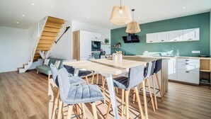 Een moderne keuken met witte kasten, een houten eettafel en een trap die leidt naar een slaapkamer op een entresol.