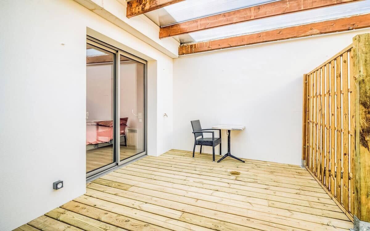 A wooden deck with a sliding glass door leading to a room with a bed and a chair.