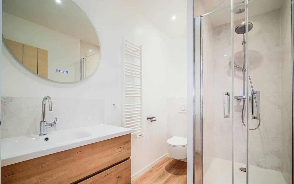 A modern bathroom with a glass-enclosed shower, a wooden vanity, and a white toilet.