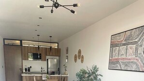 A modern living room with a dark grey sofa, a wooden coffee table with a vase and remote, and a kitchen in the background.