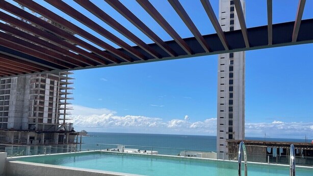A rooftop pool with a view of the ocean and a tall building in the background.