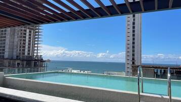 A rooftop pool with a view of the ocean and a tall building in the background.