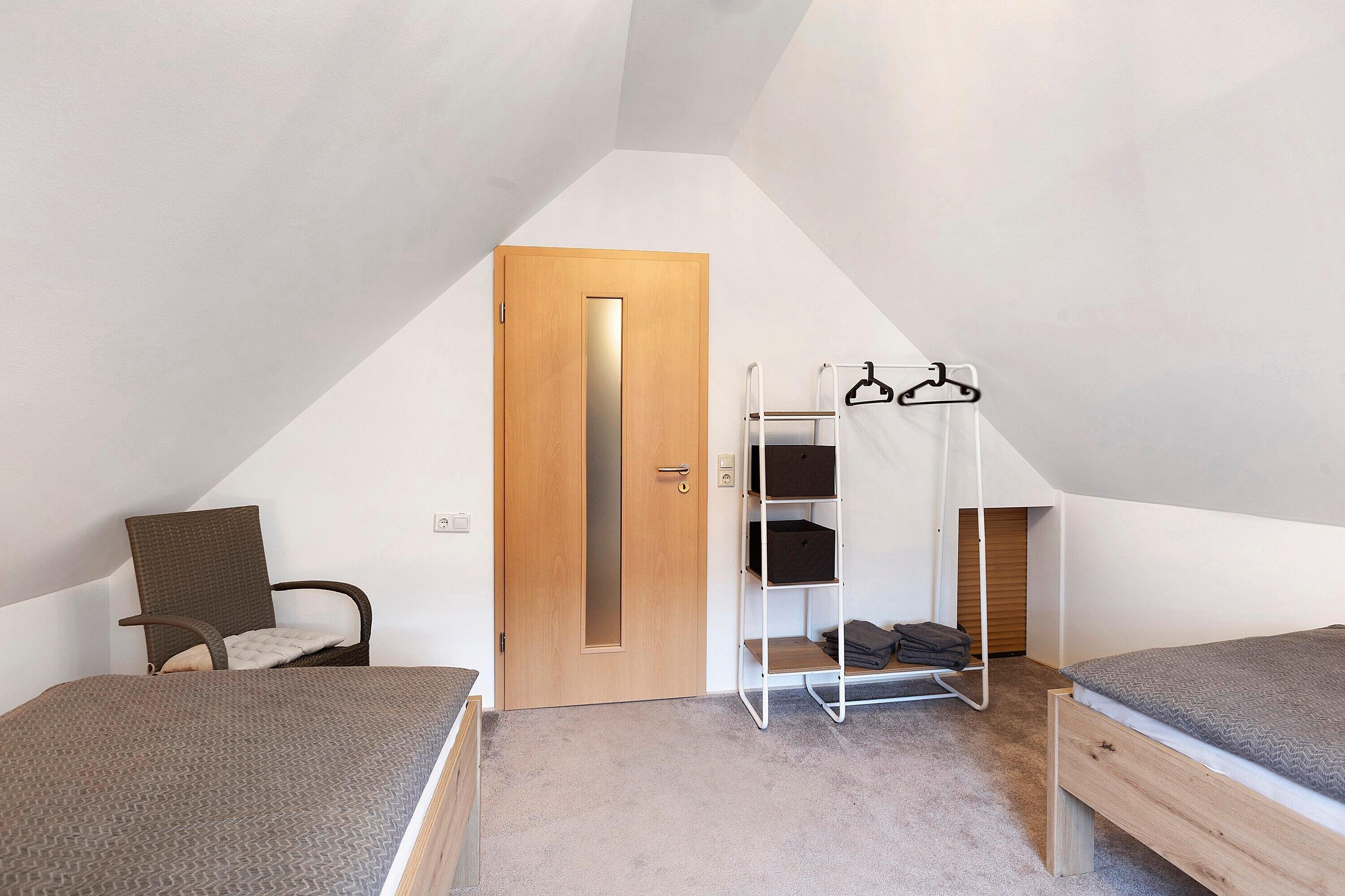 A bedroom with a wooden door, a chair, a metal shelf unit, and a bed.
