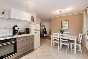 A modern kitchen with a Siemens oven, a coffee maker, and a refrigerator. There is a dining area with a table and chairs.