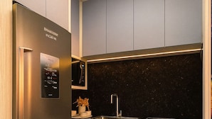 A modern kitchen with a stainless steel refrigerator, grey cabinets, a black countertop, and a marble floor. - Pousada Mar do Sul (Itapema)