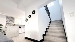 Een modern interieur met een trap die naar een tweede verdieping leidt, een keuken met witte kasten en een accentmuur van marmer.
