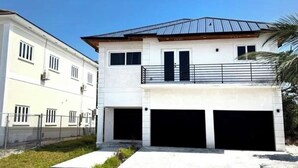 Een tweelaags huis met een witte gevel, een balkon met een metalen hekwerk en twee garage deuren.