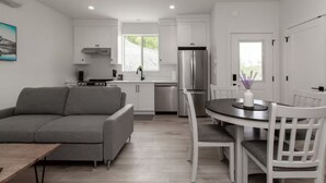 Eine moderne Küche mit weißen Schränken, einem Edelstahl-Kühlschrank und einem Essbereich mit einem runden Tisch und weißen Stühlen.