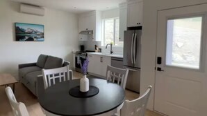 Eine moderne Küche mit weißen Schränken, einem Kühlschrank und einem Fenster. Es gibt eine Essecke mit einem runden Tisch und Stühlen.
