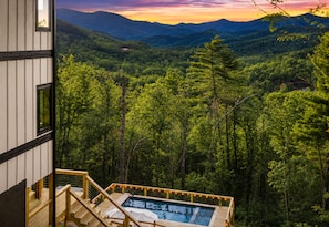 Ein Pool mit Holzterrasse und Blick auf einen bewaldeten Gebirgszug.
