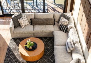 Un canapé modulable agrémenté de plusieurs coussins, une table basse ronde en bois avec une plante, et un tapis à motifs.