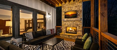 An outdoor living area with a stone fireplace, wooden deck, and seating arrangements.