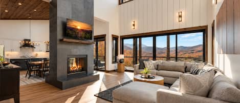 A spacious living area with a fireplace, a large sofa, and a dining area with a kitchen in the background.