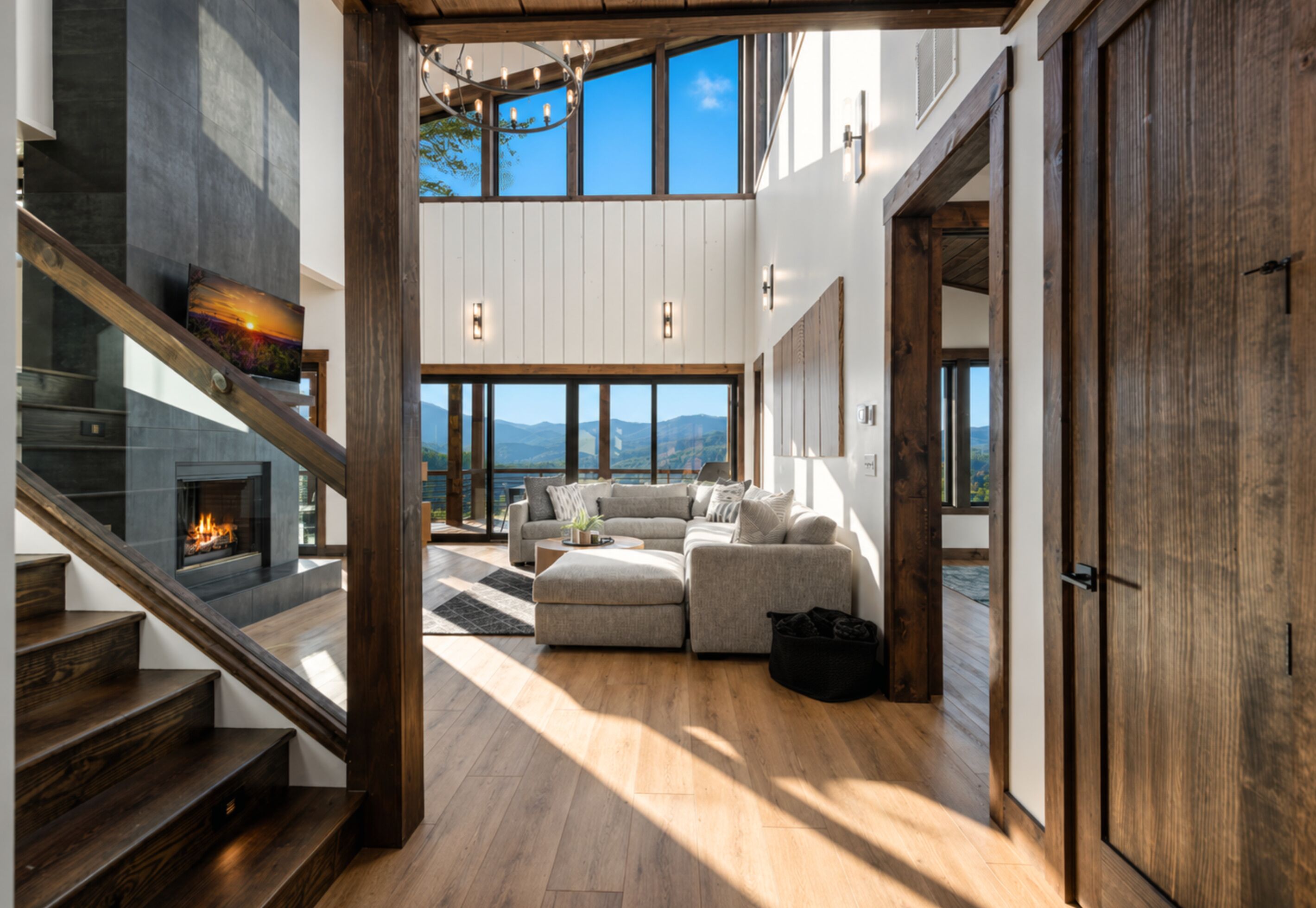 A modern interior with a staircase, a fireplace, a sectional sofa, and large windows offering a view.