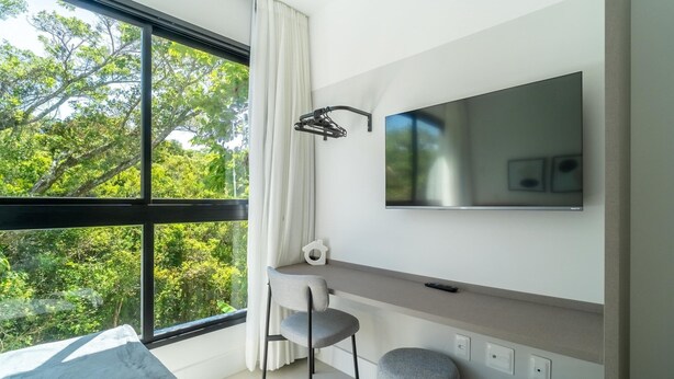 A modern room with a large window, a desk, a chair, and a mounted TV. - Modern Studios 150m From Lagoa da Conceicao - Lsts I (Florianópolis)
