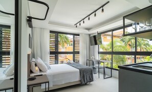 Quarto de hotel moderno com cama, mesa de cabeceira, abajur e grandes janelas com vista para o exterior.