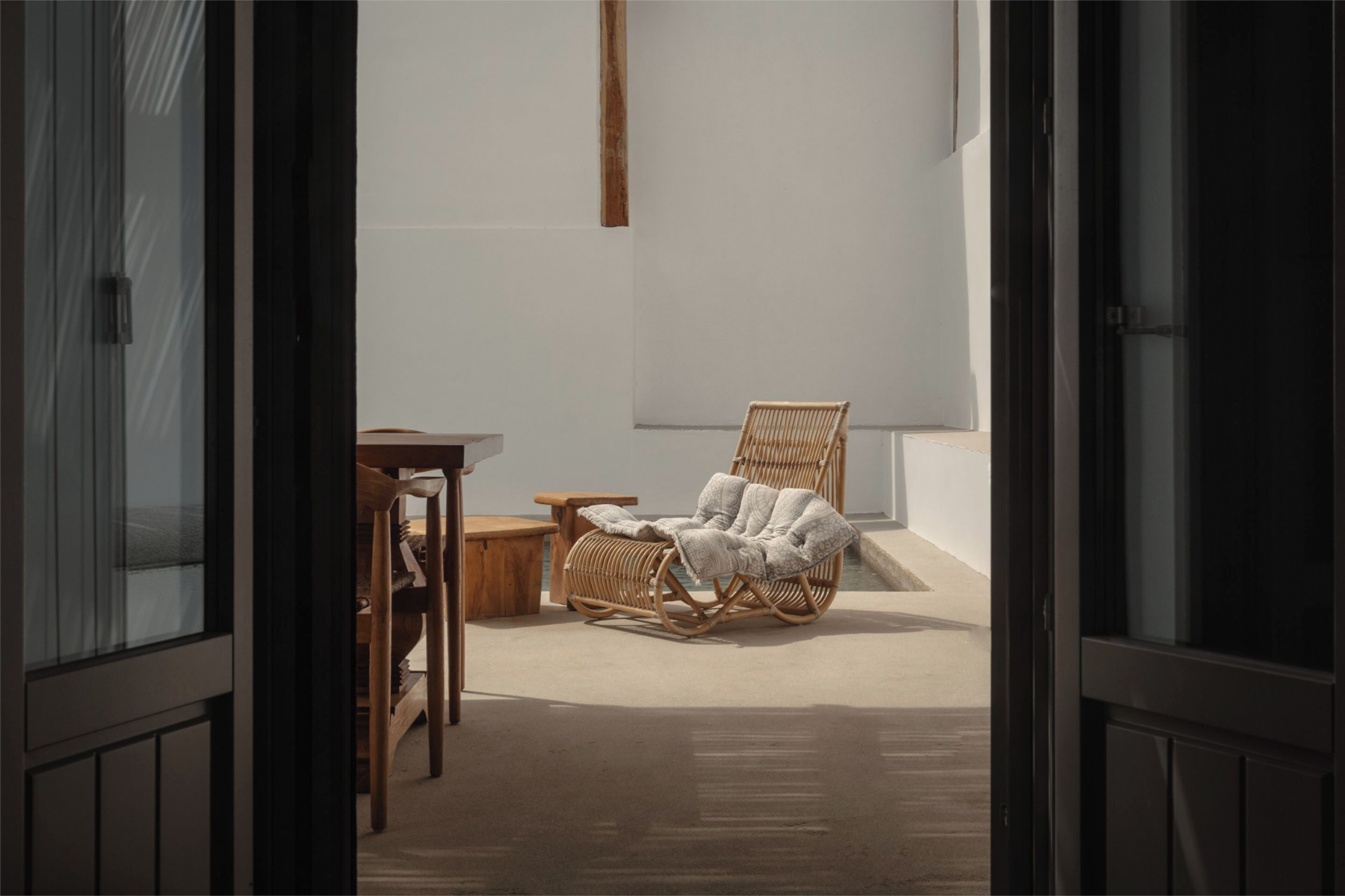 A room with a wicker chair, a wooden table, and a small stool.