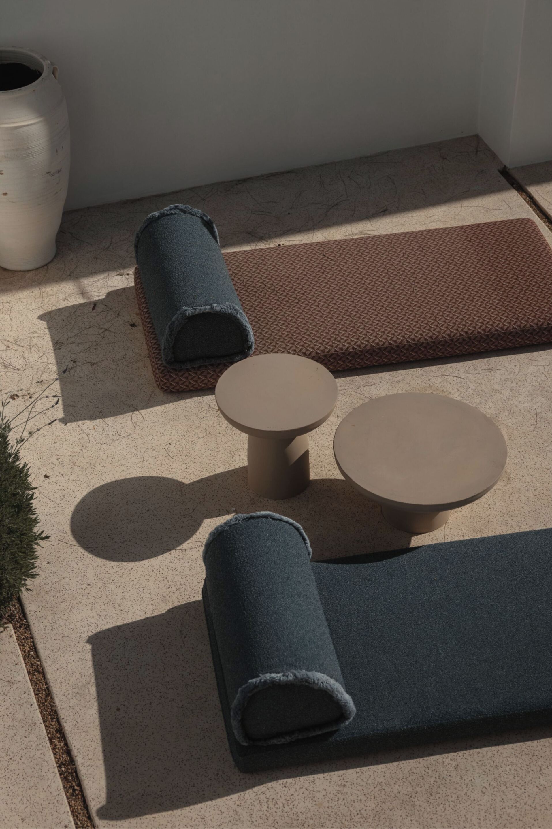A small outdoor seating area with two round tables and a bench, a textured rug, and a large white vase.