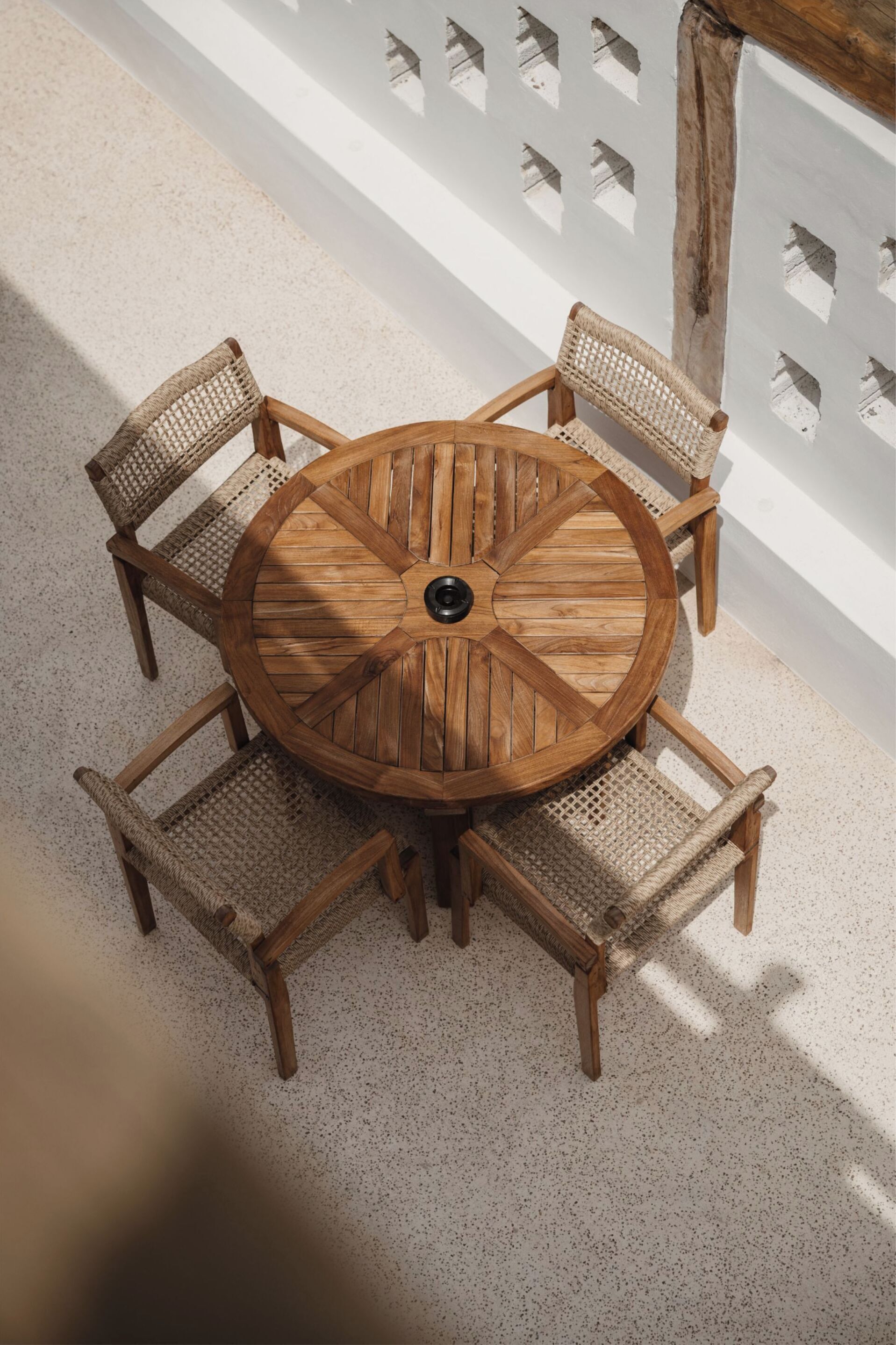A round wooden table with four woven chairs, set on a speckled floor.