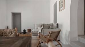 Minimalistinen olohuone, jossa on sohva, puinen sohvapöytä ja rottinkituoli.