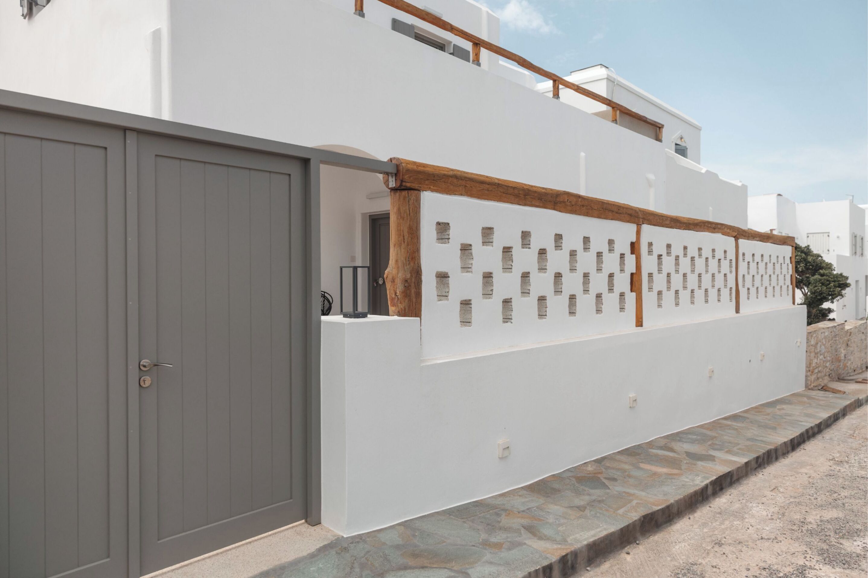 A modern building with a grey door, white walls, and a wooden fence with square cutouts.