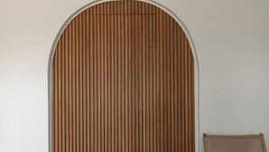 Ein Essbereich mit einer Holzwand, einem runden Tisch gedeckt mit Tellern und Gläsern sowie einem Korbstuhl.