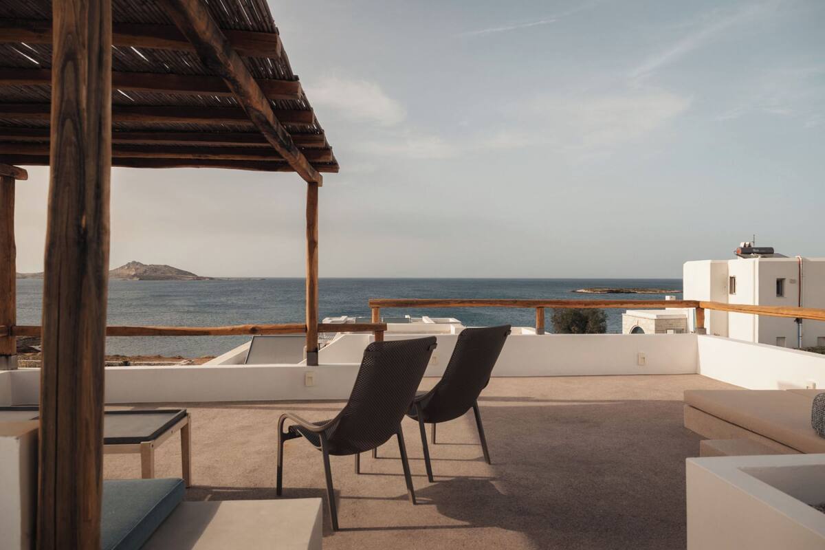 Une terrasse sur le toit, avec deux chaises, une table et une vue sur la mer et une île lointaine.
