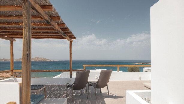 Eine Terrasse mit einer Holzpergola, zwei Stühlen, einem Tisch und Blick auf das Meer und die entfernten Hügel.