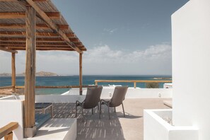 A terrace with a wooden pergola, two chairs, a table, and a view of the sea and distant hills. - Siora of Paros - Malatesta & Piccolo (Paros)