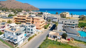 A coastal residential area with modern buildings, a road, and a mountain in the background. - Pnoe Beachside Suite (Georgioupoli)