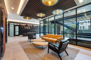 Un hall d’entrée moderne doté d’un comptoir de réception, d’un espace salon et de grandes fenêtres donnant sur l’extérieur.