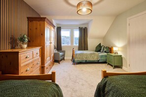 A bedroom with a large wooden dresser, a bed with green bedding, a nightstand with a lamp, and a window with curtains. - Host Stay The Annex (Jedburgh)