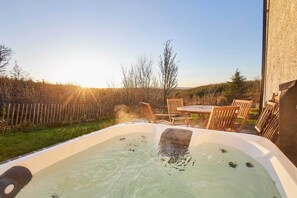 A hot tub in a backyard with a wooden table and chairs, surrounded by a wooden fence and trees. - Host Stay The Annex (Jedburgh)