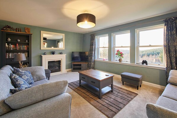A living room with a fireplace, a television, and a large window with curtains. - Host Stay The Annex (Jedburgh)