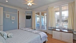 A bedroom with a bed, a ceiling fan, a TV, and a view of the outside balcony. - Beautiful Family Home with Private Pool, Hot Tub Movie Room & Rooftop Terrace! Ocean Views, Beach steps away! (Isle of Palms)