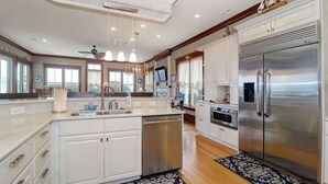 A spacious kitchen with a large stainless steel refrigerator, white cabinetry, and a central island with a dishwasher. - Beautiful Family Home with Private Pool, Hot Tub Movie Room & Rooftop Terrace! Ocean Views, Beach steps away! (Isle of Palms)