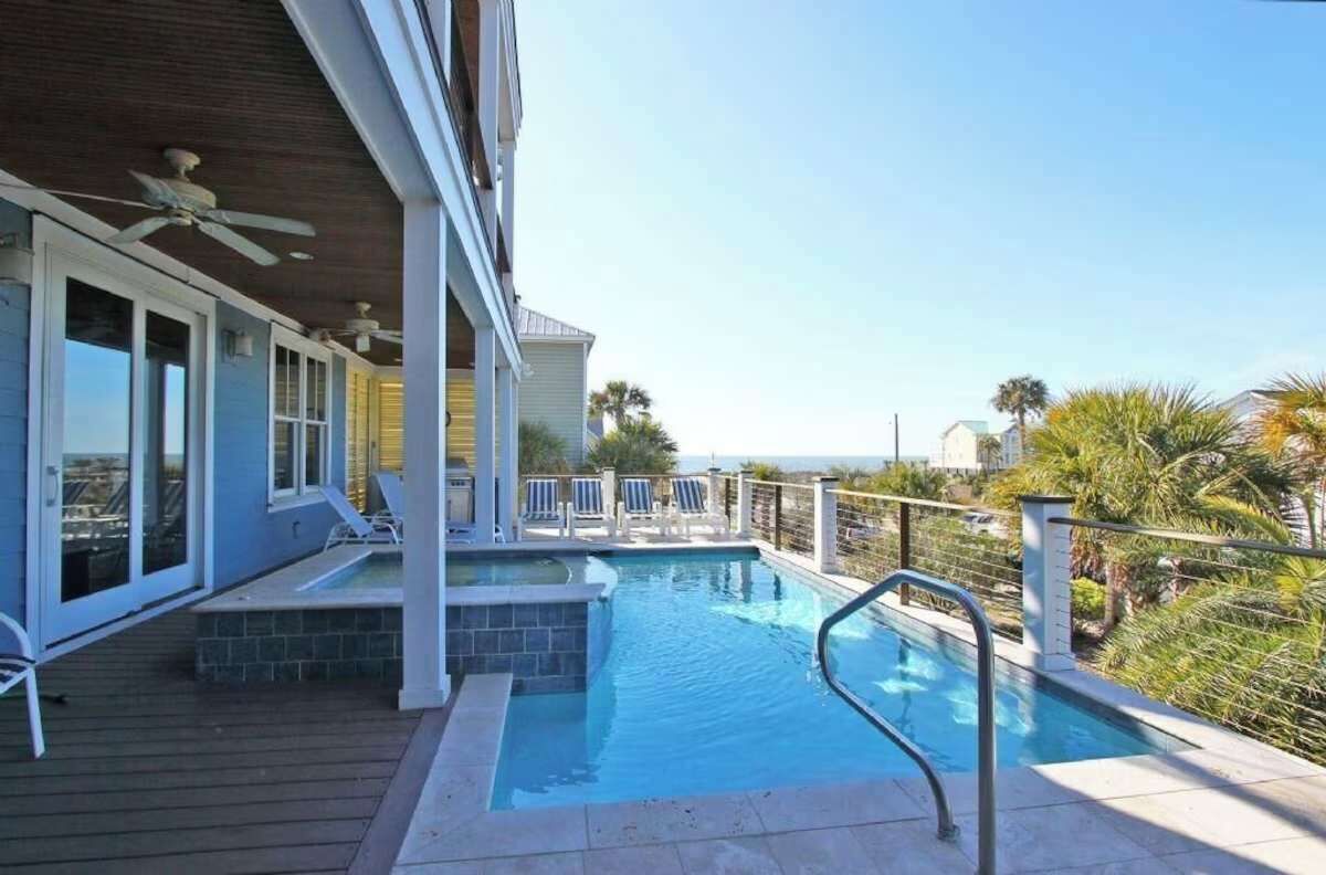 A swimming pool with lounge chairs and a deck, surrounded by palm trees and a clear sky.