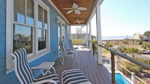 A covered porch with striped chairs and a ceiling fan, overlooking a beach and ocean view. - Beautiful Family Home with Private Pool, Hot Tub Movie Room & Rooftop Terrace! Ocean Views, Beach steps away! (Isle of Palms)