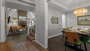 A spacious living area with a fireplace, a dining table set for four, and a staircase leading to an upper level. - NEW: Big House, 13 beds, 6 bedroom, 17 min to DT (Overland Park)