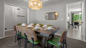 A dining room with a wooden table set for four, green chairs, a hanging light fixture, and a mirror on the wall. - NEW: Big House, 13 beds, 6 bedroom, 17 min to DT (Overland Park)