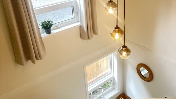 A staircase with a view of a window and a hanging light fixture.