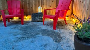 Two red Adirondack chairs with a lantern and a potted plant in a wooden-fenced outdoor area.