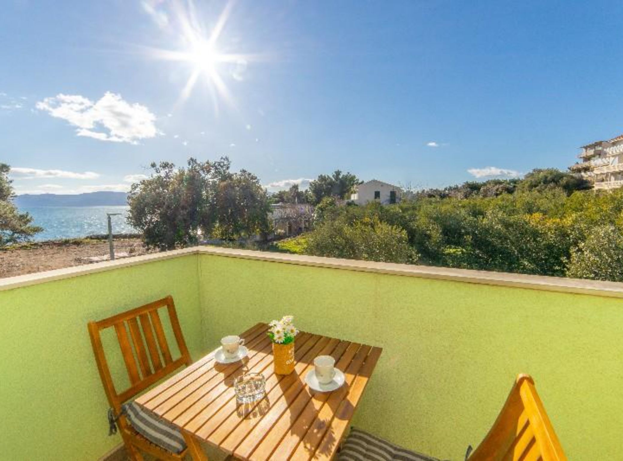 A balcony with a wooden table, two chairs, and a small table setting with a cup and a vase of flowers.