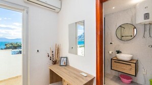 Een moderne badkamer met een houten wastafel, een ronde spiegel en uitzicht op zee.