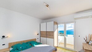 Een slaapkamer met een bed, een kledingkast, een bureau en uitzicht op zee.