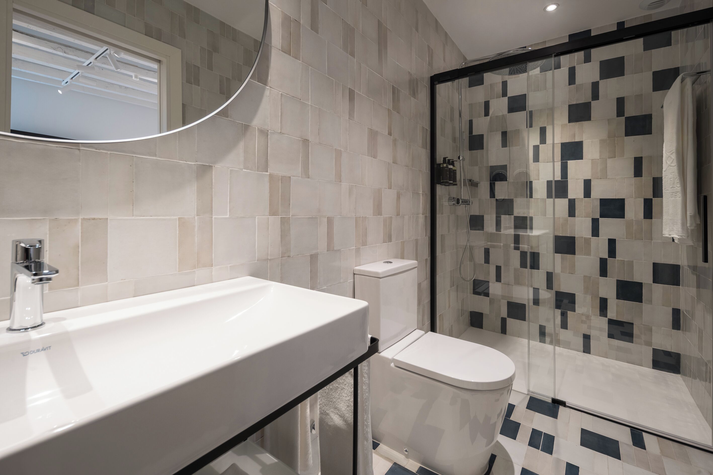 A modern bathroom with a white sink, toilet, and glass shower enclosure.
