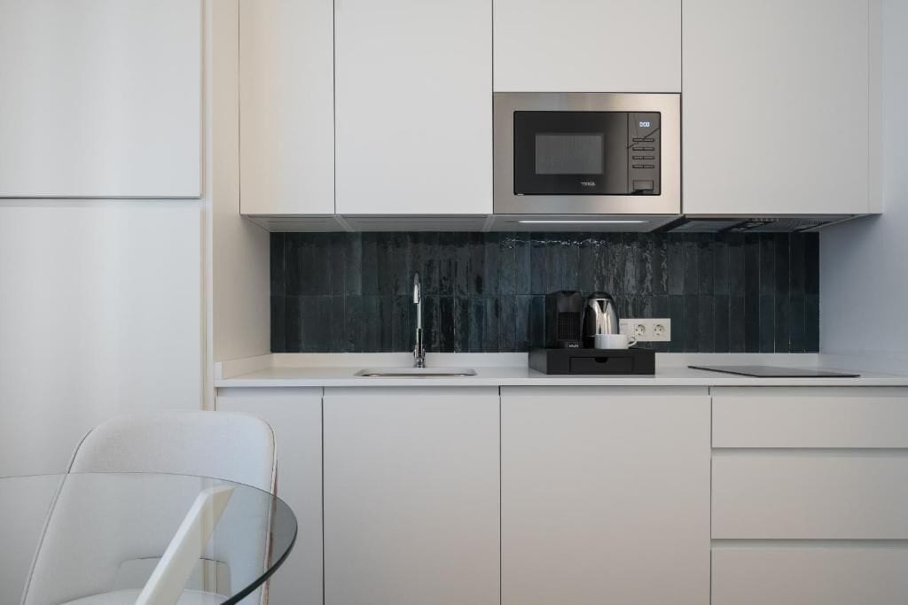 A modern kitchen with white cabinetry, a stainless steel microwave, and a coffee machine on the countertop.