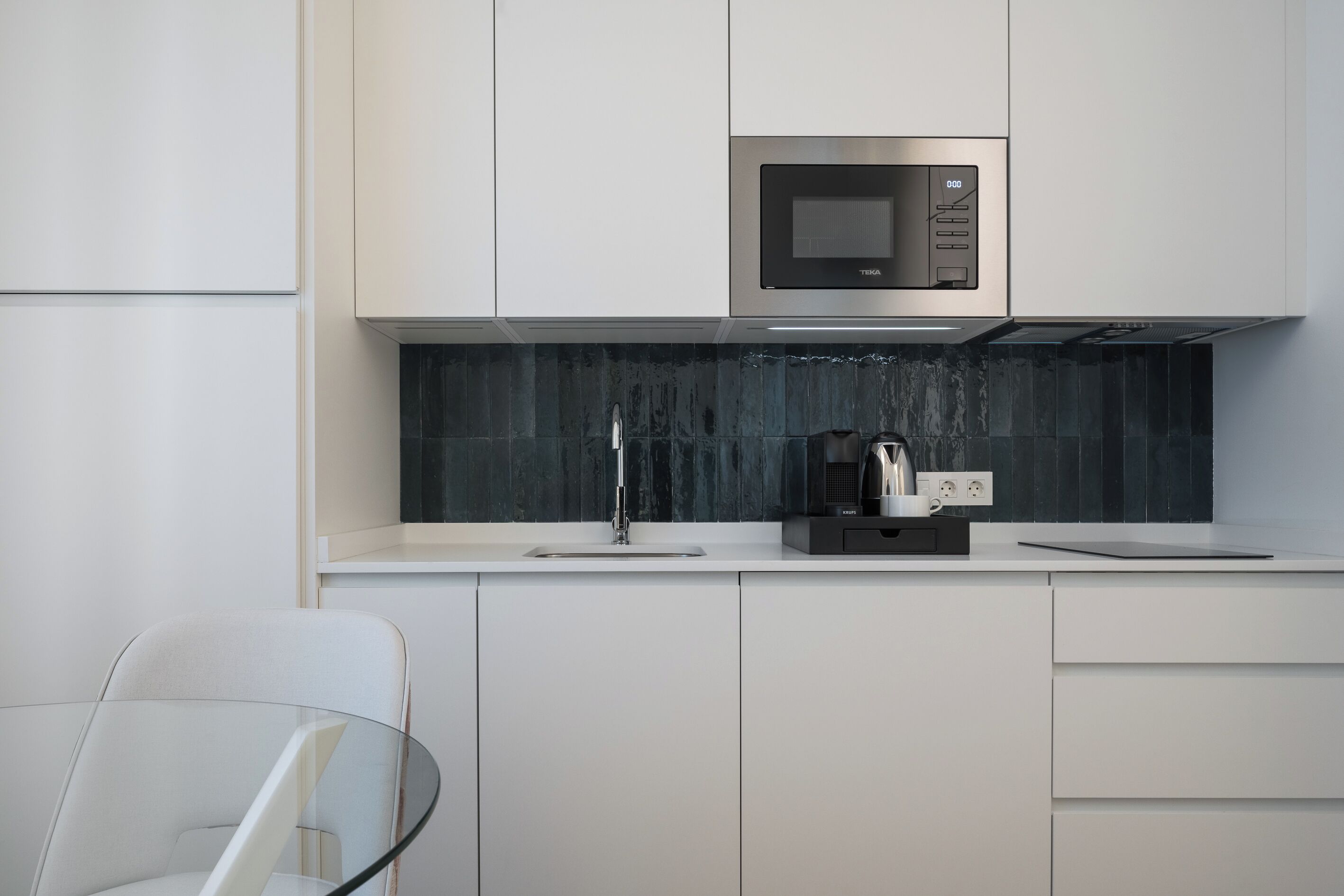 Una cocina moderna con armarios blancos, salpicadero negro y microondas integrado.