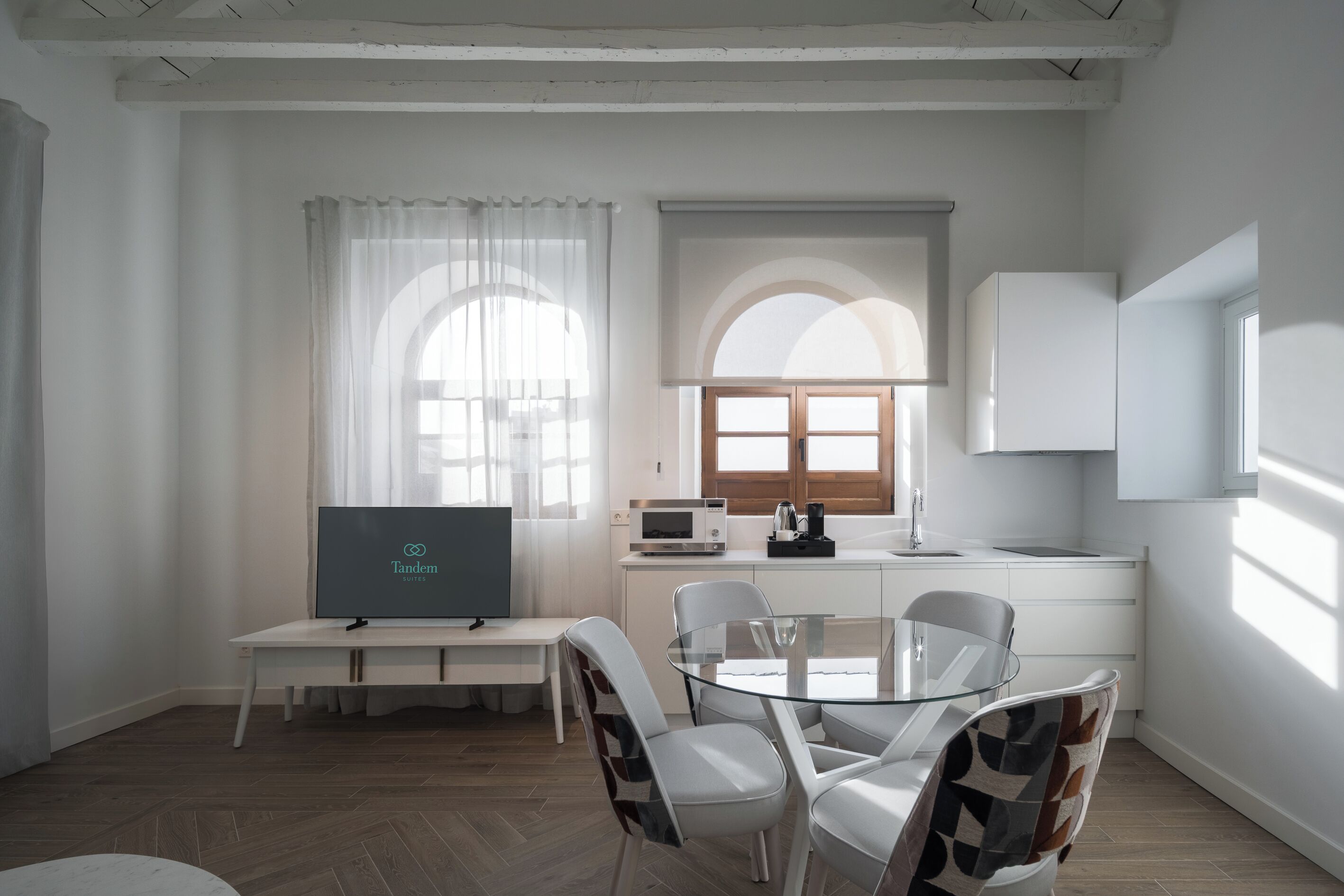 A modern, well-lit room with a dining table, chairs, a TV, a microwave, and a window with curtains.