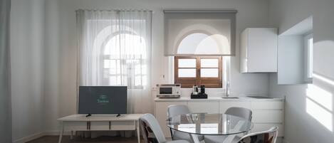 A modern, well-lit room with a dining table, chairs, a TV, a microwave, and a window with curtains.